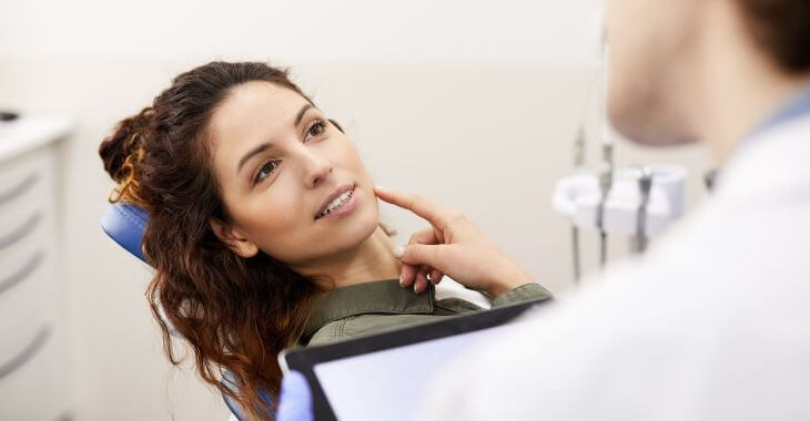 A concerned woman pointing at her mouth talking to a dentist.