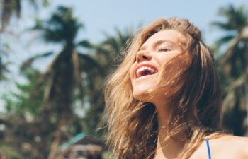 Beauty Sunshine Girl Portrait. Pretty happy woman enjoying summer outdoors. Sunny Summer Day under the Hot Sun on the Beach.